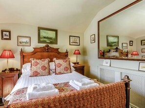 Une chambre d’hôtel avec un grand lit, deux tables de chevet avec des lampes, un grand miroir et des tableaux encadrés aux murs.