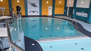 Sisätiloissa sijaitseva uima-allas, jossa on kirkasta vettä, hyppytorni ja seinässä kyltti, jossa lukee ”uinti sallittu”.