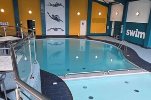 An indoor swimming pool with clear water, a diving board, and a 'swim' sign on the wall.