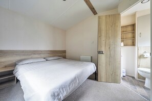 A bedroom with a bed, a wooden headboard, a radiator, and a bathroom with a toilet and a shelf.