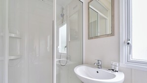 A bathroom with a glass shower enclosure, a white sink with a mirror above it, and a window.