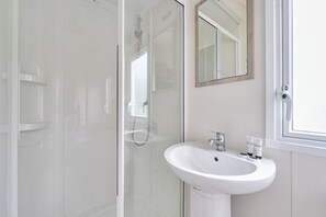 A bathroom with a glass shower enclosure, a white sink with a mirror above it, and a window.
