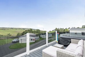A balcony with wicker furniture, a view of a road, and a grassy field.
