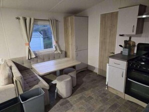 A compact kitchen with a dining area, a window with curtains, and a stove.