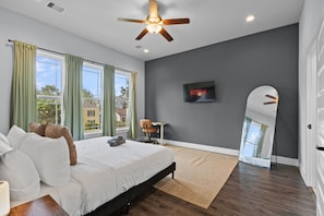 A bedroom with a bed, a ceiling fan, a TV, a chair, and a large window with curtains. - 15 Mins NRG, Modern Home w/ 3 King Suites & Garage (Houston)