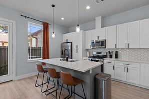 A modern kitchen with white cabinets, a central island with bar stools, stainless steel appliances, and pendant lighting. - 15 Mins NRG, Modern Home w/ 3 King Suites & Garage (Houston)