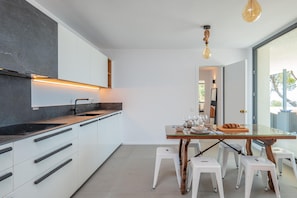 Eine moderne Küche mit weißen Schränken, einer schwarzen Arbeitsplatte und einem Glastisch mit Barhocker.