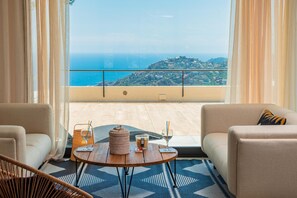 A balcony with a view of the sea and hills, furnished with a sofa, a round table, and a chair.