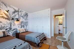 Ein Schlafzimmer mit zwei Betten, einem Kleiderschrank, einem Sessel und einer Wand mit Pflanzenmotiv.