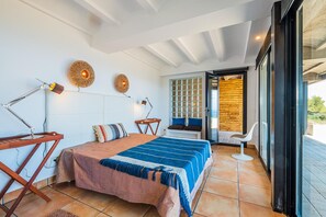 A bedroom with a bed, bedside lamps, a window with blinds, and a view of the outdoors.