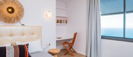 A bedroom with a bed, a desk, a chair, a round wall decoration, and a large window.