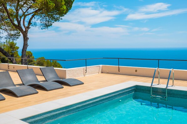 A poolside area with lounge chairs, a pool, and a view of the ocean.