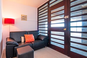 A room with a black leather sofa, a red floor lamp, and a wooden door with glass panels.