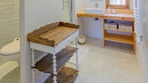 A bathroom with a wooden vanity, a mirror, a window, and a tiled floor. - Le Tinailler - PRISSE (PRISSE)