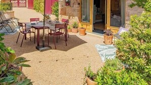 A two-story building with a balcony, a patio with a table and chairs, and potted plants. - Le Tinailler - PRISSE (PRISSE)