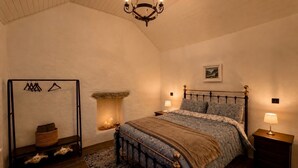 A bedroom with a bed, a hanging light fixture, a fireplace, and a wooden floor.