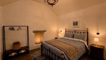 A bedroom with a bed, a hanging light fixture, a fireplace, and a wooden floor.