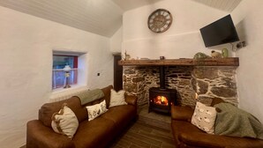 A cozy living room with a stone fireplace, a mounted TV, and a window with a view.