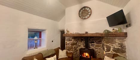 A cozy living room with a stone fireplace, a mounted TV, and a window with a view.