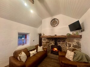 A cozy living room with a stone fireplace, a mounted TV, and a window with a view.