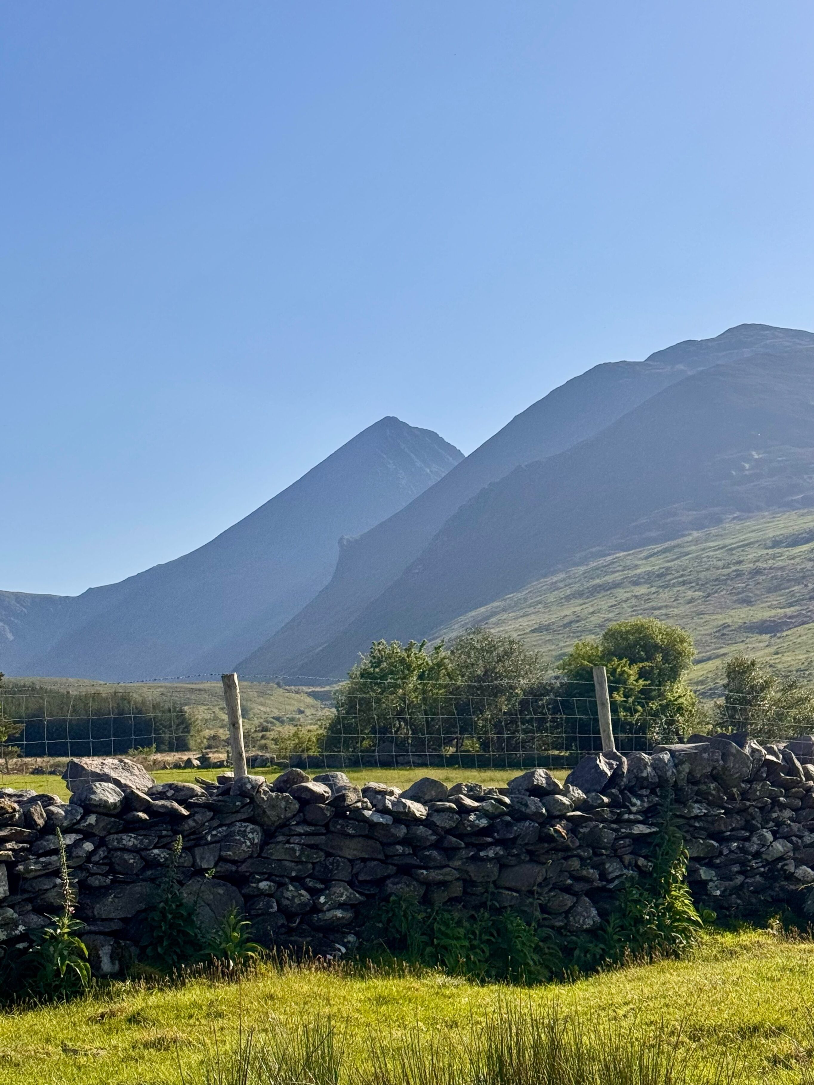 Un mur de pierre, un champ d’herbe et une chaîne de montagnes.