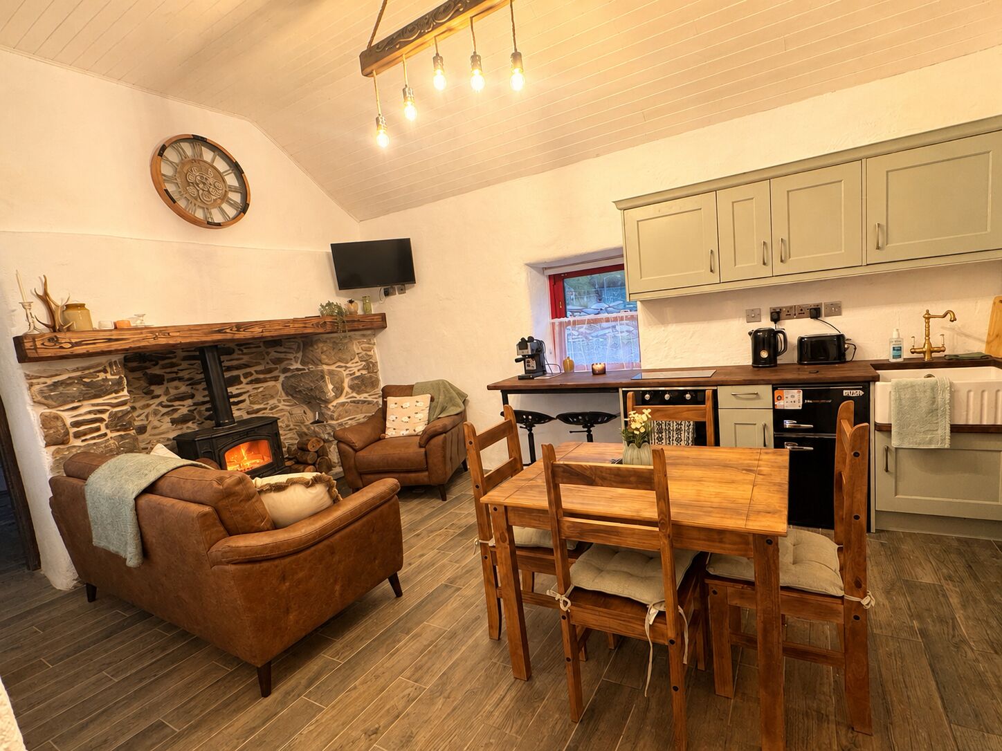 A cozy living room with a stone fireplace, a television mounted on the wall, and a dining area with wooden furniture.