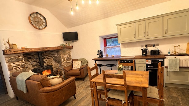 A cozy living room with a stone fireplace, a television mounted on the wall, and a dining area with wooden furniture.