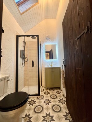 A bathroom with a shower, toilet, and sink, featuring a geometric tile floor and a wooden door. - Cottage Sleeps 4 with Parking (Killarney)