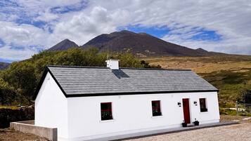 A white building with a red door, a grey roof, and a stone wall in the foreground.