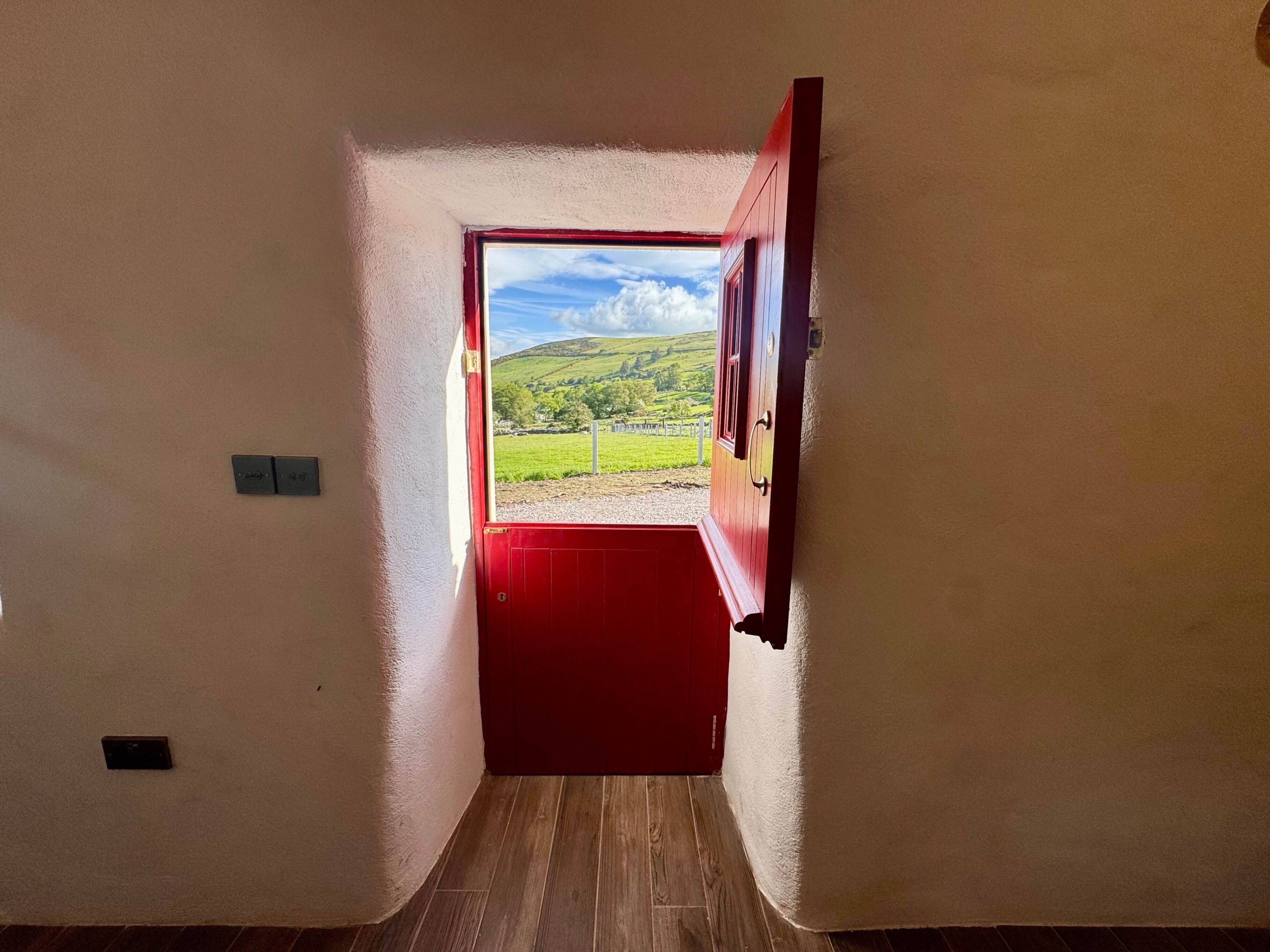 A hallway leading to a red door with a view of a green landscape.
