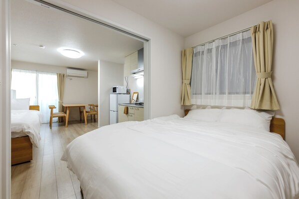 A hotel room with a bed, a desk, a chair, a kitchenette, and a bathroom.