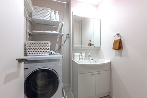 A compact laundry area with a washing machine, shelves with laundry baskets, a sink, and a mirror.