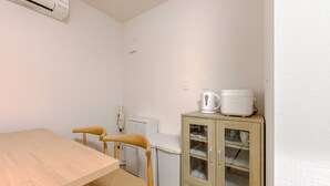 A small room with a wooden table, a chair, a cabinet with glass doors, a white kettle, and a small white appliance. - Kasatori-cho I [9-minute drive from Nagoya Station] Newly Built 1LDK / WiFi Included / Full Amenities / Sleeps Up to 3 / Ideal for Sightseeing / 1-101 (Kasatori-cho, Nishi-ku, Nagoya City,)