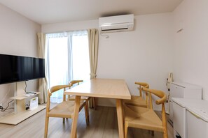 Et værelse med et træbord, fire stole, et fladskærms-tv, en aircondition og et hvidt køleskab.