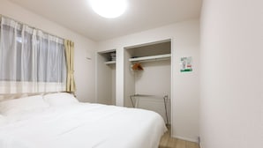 A bedroom with a bed, a window with sheer curtains, a radiator, and a closet with shelves. - Kasatori-cho I [9-minute drive from Nagoya Station] Newly Built 1LDK / WiFi Included / Full Amenities / Sleeps Up to 3 / Ideal for Sightseeing / 1-101 (Kasatori-cho, Nishi-ku, Nagoya City,)