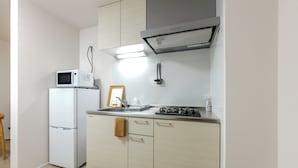 A compact kitchen with a microwave, stove, and a framed picture on the counter. - Kasatori-cho I [9-minute drive from Nagoya Station] Newly Built 1LDK / WiFi Included / Full Amenities / Sleeps Up to 3 / Ideal for Sightseeing / 1-101 (Kasatori-cho, Nishi-ku, Nagoya City,)