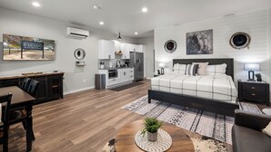Une chambre moderne avec un grand lit, un coin repas avec une table et des chaises, une cuisine avec des meubles blancs et un salon avec un canapé et une table basse.