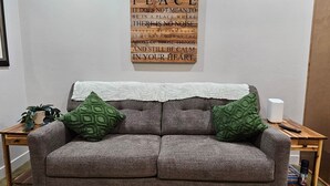 A grey sofa with green cushions, a white wall, and a wooden plaque with a peace quote. - Saguaro Grove, Built May '26, Smart Lock, Quiet Cul-de-sac (Tucson)