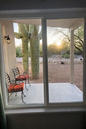 A room with a sliding glass door leading to an outdoor patio with a cactus and chairs.