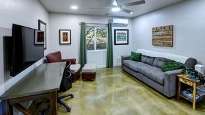 A living room with a sofa, a coffee table, a TV, a ceiling fan, and a window with curtains. - Saguaro Grove, Built May '26, Smart Lock, Quiet Cul-de-sac (Tucson)