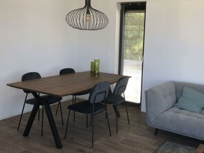 A dining area with a wooden table, black chairs, a hanging light fixture, and a window with blinds. - Holiday Home in Enkhuizen With Terrace (Enkhuizen)