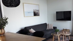 A modern living room with a sofa, a dining table, a TV, and a framed picture on the wall.
