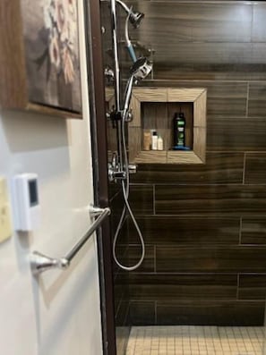 A shower with a wooden shelf containing toiletries.