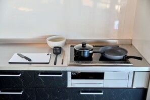 A kitchen with a stove, a pot, a frying pan, a cutting board, a knife, and a bowl.