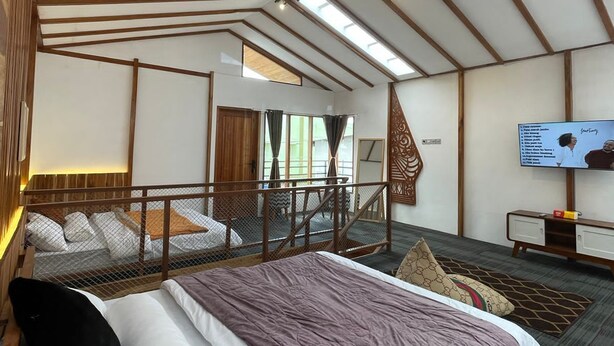 Una habitación amplia con techo alto, una cama con cabecera, un televisor y una escalera que conduce a un nivel superior.