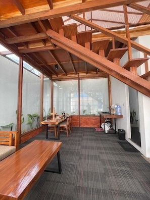 A room with a wooden ceiling structure, a dining table, chairs, a small kitchen area, and large windows. - Villa Sampai Dieng (Dieng Kulon)