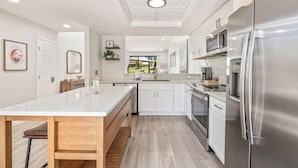 Une cuisine moderne avec des meubles blancs, des appareils en acier inoxydable et une table à manger en bois.