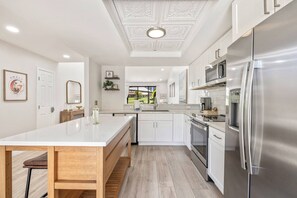 A modern kitchen with white cabinetry, stainless steel appliances, and a wooden dining table. - *Palm Valley CC, 76643 Daffodil Dr (Palm Desert)