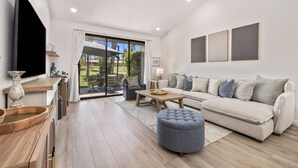 Un salon moderne avec un canapé, un pouf et un téléviseur posé sur un meuble en bois.