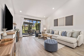 A modern living room with a sofa, ottoman, and a TV on a wooden stand. - *Palm Valley CC, 76643 Daffodil Dr (Palm Desert)